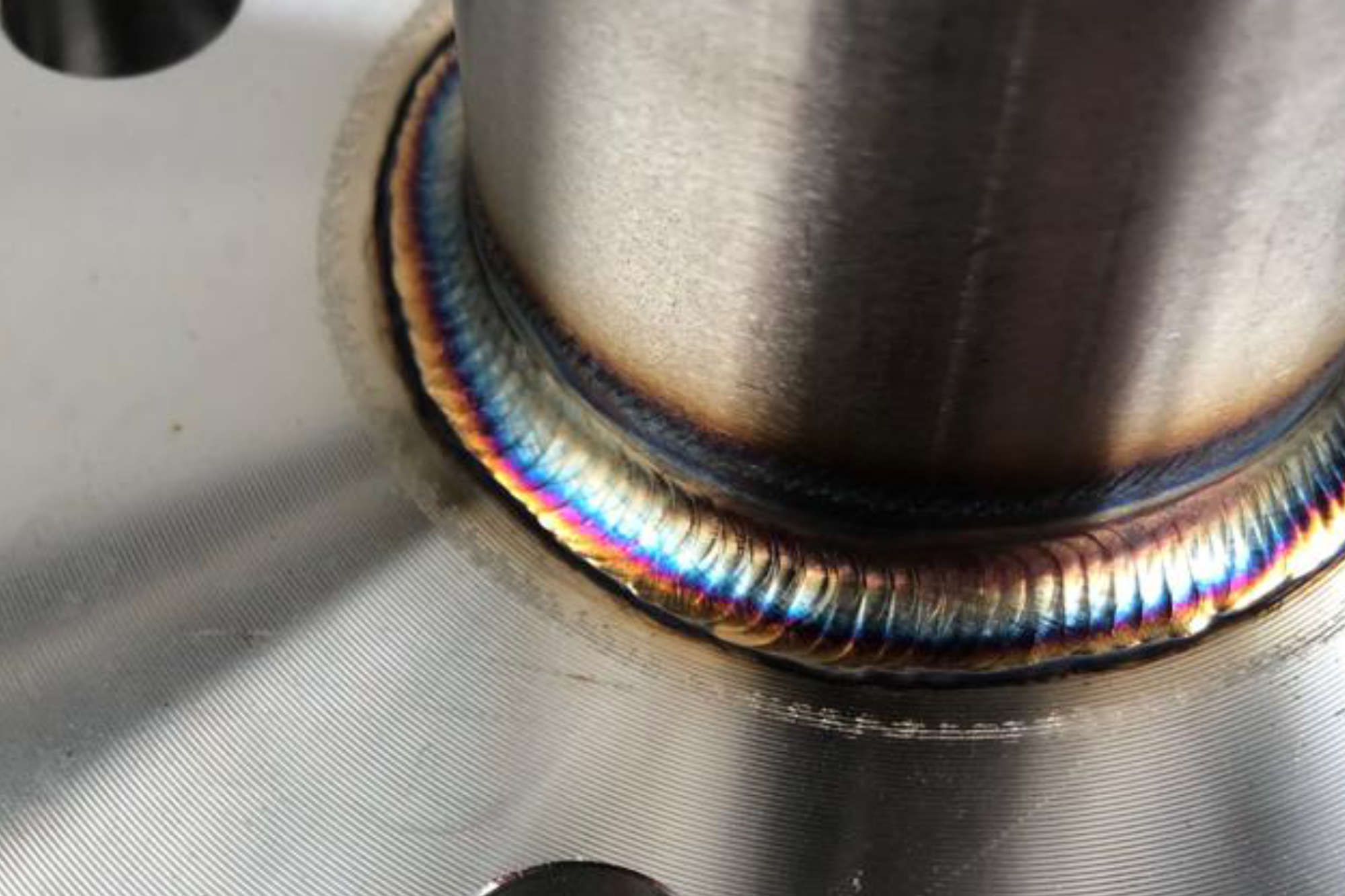 Soldadura de precisión en junta de tubería de acero inoxidable mostrando cordón uniforme y zona afectada por el calor con tintes de color.